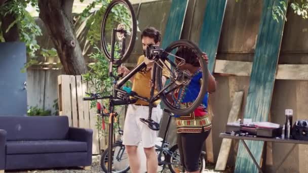决心与外界热爱运动的夫妇一起重新调整和调整损坏的自行车 年轻的高加索男子帮助黑人妇女搬运和夹住自行车修理站的车辆 — 图库视频影像