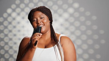 Happy young woman singing at hair brush in studio, enjoying skincare ad campaign and feeling confident. Beautiful smiling girl having fun with music, acting silly and laughing.