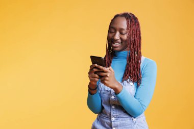 Tatil gezisinde cep telefonu kullanan Afrikalı Amerikalı bir kız, stüdyoda sosyal medya uygulamalarına göz atıyor. Akıllı telefondan internet sayfasına, hafta sonu aktivitelerine bakan genç.