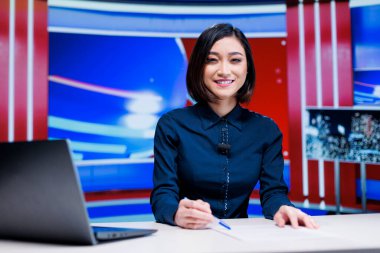Haber odasındaki Asyalı sunucu, canlı yayında en son uluslararası olaylardan bahsediyor. Medya manşetleriyle televizyon içeriği yaratan kadın muhabir.