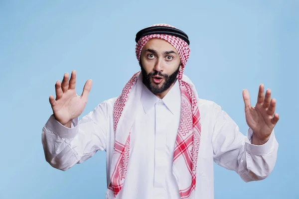 兴奋的男人举手表决穿上传统的穆斯林服装 说着工作室的肖像 戴阿拉伯头巾的人 一边说话一边看着相机 一边摆出姿势 — 图库照片