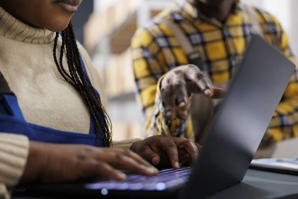 African american woman warehouse worker hands typing on laptop. Storehouse employee checking stock supply schedule online, using goods inventory management computer software close up