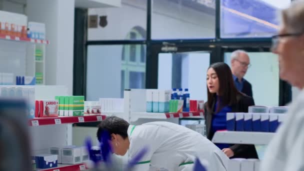在药房里的亚洲妇女需要处方药来对抗病毒 要求药剂师帮助她选择最好的药物 协助客户处理产品糖分的药剂技师 — 图库视频影像