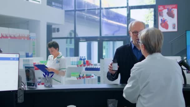 薬品の在庫を確認する資格のある化学者にリダイレクトするキャッシャーからの援助を要求する鎮静剤で処方薬の情報を必要とする高齢男性 — ストック動画
