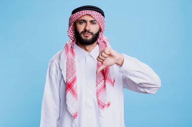 Geleneksel giysiler giyen ciddi bir Arap jest stüdyosu portresiyle poz veriyor. Beyaz İslami cüppeli ve türbanlı müslüman bir insan anlaşmazlık jesti yapıyor ve kameraya bakıyor.