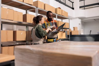 Depo çalışanları karton kutuları nakliyeye hazırlamak için dijital tablet üzerindeki kontrol listesini kullanarak paketi arıyorlar. Girişimci tulum giyer, karton kutuyu tarayıcı kullanarak tarar.