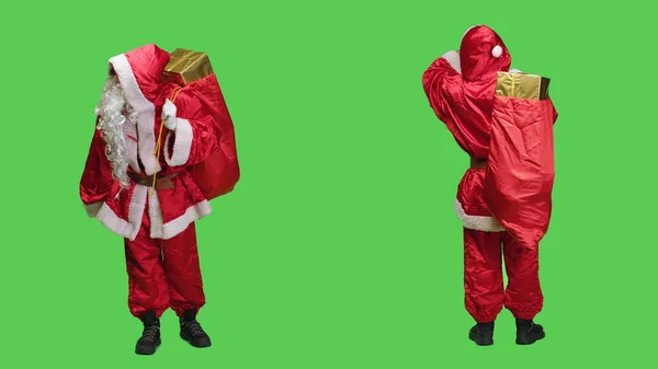 圣诞老人在工作室里四处张望 带着装满礼品盒的大袋子走过全身绿屏 年轻人装扮成圣诞老人 散发圣诞气息 给孩子们送礼物 — 图库照片