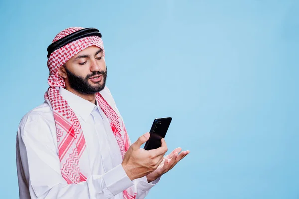 身着传统服装的穆斯林男子在智能手机上通过视频聊天 进行远程连接 在网上会议上使用手机交谈的贫民区和原址的阿拉伯人 — 图库照片