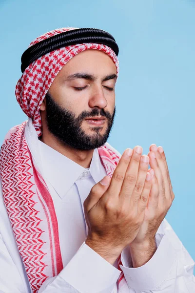 Gözü kapalı dindar Müslüman adam kollarını açıp Tanrı 'ya dua ediyor. Ganutra başlık ve cübbe giymiş Arap adam ibadet ve inanç kavramını gösteren geleneksel giysiler giyiyor.