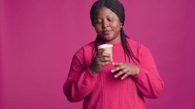 Afro-Amerikan kadın portresi. Düşüncelerinde yukarı bakıyor ve elinde kahve tutuyor. Pembe kazak giyen kadın moda blogcusu sıcak içecekten hoşlanıyor.