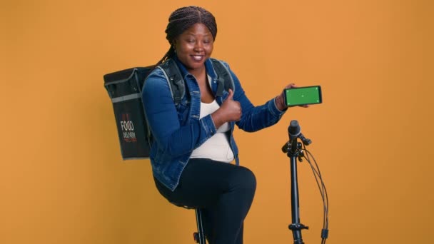 非洲裔美国人信使抓起手机 骑自行车时显示绿色屏幕显示 黑人妇女演示了带隔离模型模板的移动设备上的尖端交付应用程序 — 图库视频影像