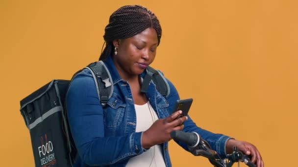 专业的黑人妇女不费吹灰之力地利用技术提供快速 无害生态的食品 年轻可靠的骑自行车的信使在路上用智能手机通过城市 — 图库视频影像