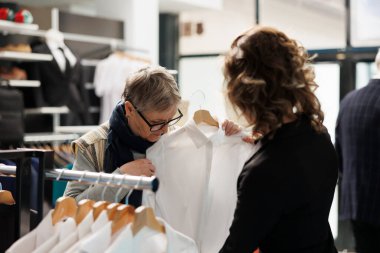 Moda kıyafetler almak isteyen yaşlı bir müşteri, mağaza çalışanından alışveriş merkezinde resmi giysiler için yardım istiyor. Son sınıf öğrencisi kadın modern butikte yeni koleksiyon ve şık aksesuarlar alıyor.