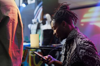 Genç Afrikalı Amerikalı bir adam gece kulübünde dinlenirken akıllı telefon kullanıyor. Kulüpte diskotek partisinde rahatlarken sosyal medyada ve cep telefonunda çevrimiçi sayfalarda gezinen kulüp üyesi