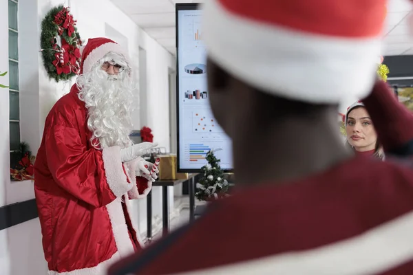 サンタクロースとして着飾られた公衆スピーカーは お祝いの装飾オフィスでキャリアを進めるために従業員を鼓舞します コワーキングミーティング参加者は ホリデーシーズン中に重要な業界スキルを学ぶ — ストック写真