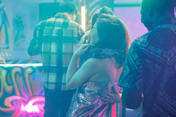 Women hugging in nightclub while attending discotheque party. Girlfriends embracing on dancefloor with spotlights while dancing and enjoying nightlife entertainment in club at night