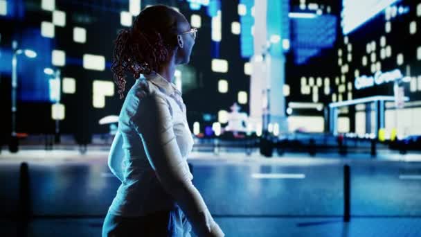 深夜时分 在城市林荫大道上徘徊的非洲裔美国女人微笑着 指着摩天大楼上有趣的广告牌 女商人在灯火通明的街道上徘徊 — 图库视频影像