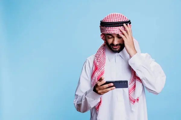 令人失望的是 Arab在工作室享受数字娱乐的同时却输掉了手机游戏的竞争 不快乐的穆斯林男子在智能手机上玩电子游戏 表情很沮丧 — 图库照片