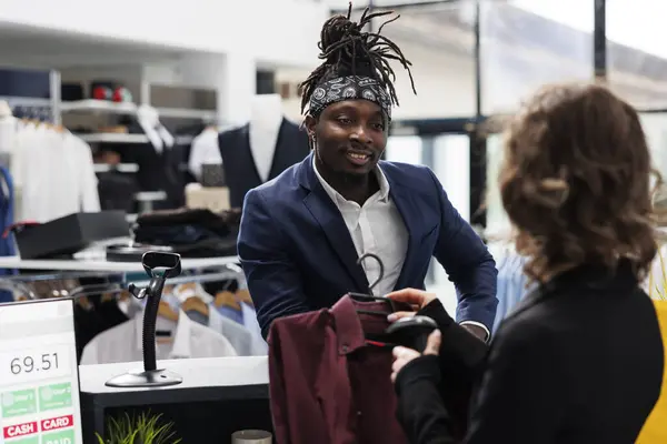 Stylish employee scanning elegant shirt using store scanner, preparing purchase for african american customer. Fashionable man buying trendy merchandise and clothes in shopping center