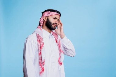 Geleneksel giysiler giyen Müslüman adam migrenden muzdarip ve tapınağı ovuyor. Baş ağrısı çekerken ve stüdyoda poz verirken başörtüsü ve başörtüsü takan Arap biri.