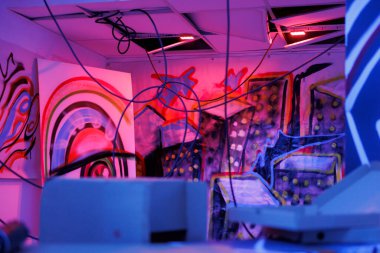 Harabelerin ve parçalanmaların karanlığında parlayan mor ve pembe ışıklarla yıkılmış eski bir bina. Paslı duvarları ve floresan neon ışığı olan dağınık terk edilmiş bir depo..