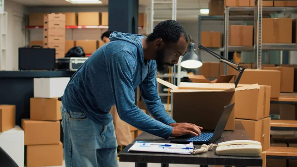 Startup partner arranging products in cardboard boxes, putting products in packages for shipment. Male entrepreneur using goods and supplies from storehouse racks, raw materials.
