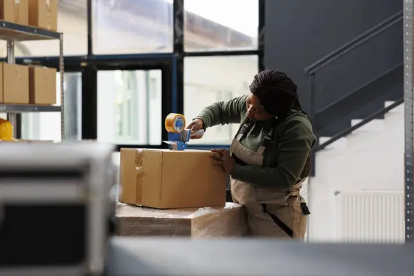 非裔美国人主管在仓库里使用胶粘带 按客户的要求工作 库房员工准备客户包裹 在库房盘点过程中检查产品 — 图库照片