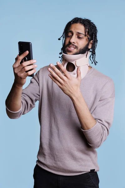 有颈圈的阿拉伯患者在智能手机上与医生进行在线咨询 戴颈架的男人在智能手机上与全科医生谈论创伤 — 图库照片