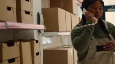 Lojistik koordinatörü ve depo toplayıcısı teslimat için sipariş hazırlıyor, karton paketlerdeki etiketleri tararken perakende deposundan telefon alıyor.