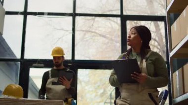 Depoda çalışan işçilerin görüntülerini izleyerek online alışveriş sitesine güncellenmiş ürünler girerek depo koridorlarında yürüyerek malların etiketlerini inceleyerek.