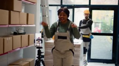 Sosyal medya platformları için video yapmak için tripoda yerleştirilmiş akıllı telefonu kullanarak depo pazarlama yöneticisi. Afro-amerikan reklam uzmanları depolama merkezinde kendi filmlerini çekiyor.