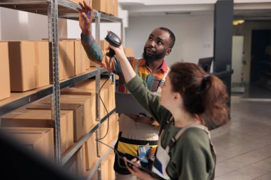 Depo amiri, müşteri paketini depoda bulmak için cihazda iş arkadaşının fatura kodunu gösteriyor. Nakliye çalışanları lojistik raporlarını incelerken ürünleri tarıyorlar.