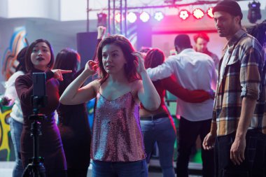 Genç bir kadın kulüpteyken akıllı telefondan tripodla selfie çekiyor. Kafkas kız gece kulübü diskoteğinde parti yapıyor ve sosyal medyada canlı yayın festivali için cep telefonu kullanıyor.