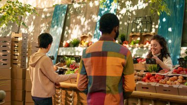 Çeşitli aileler yerel pazar yerinde sebze alışverişi yapıyor ve yerel olarak yetişen organik ürünlere bakıyorlar. Neşeli insanlar tezgahta çiftçi market sahipleriyle konuşuyor..