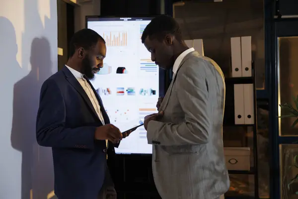 Workers looking at financial statistics on presentation board, discussing company investment strategy working late at night in startup office. Executive managers brainstorming management ideas.