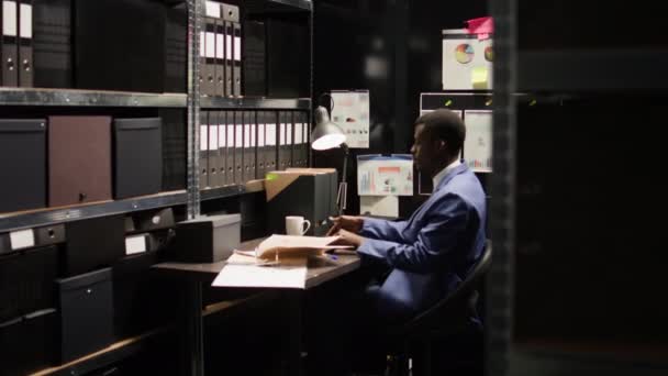 男性の私立探偵は 彼のパソコンを梱包して閉鎖した後 オフィス室を出ます アフリカ系アメリカ人の警察官が机を設置し 書類を整理し ラップトップバッグを運ぶ — ストック動画