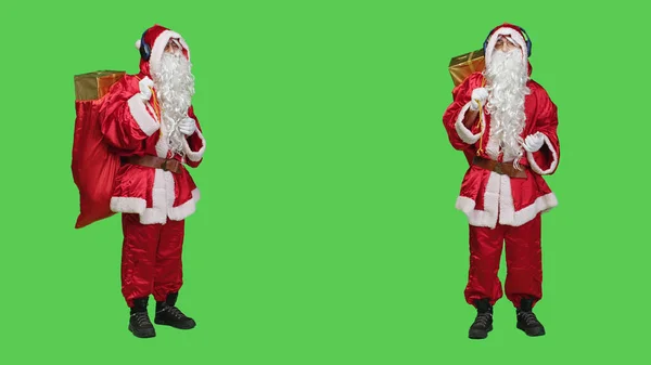 Young man dancing on songs in studio, acting like father christmas and listening to music on headphones. Modern saint nick character enjoying dance moves with audio headset, red costume.