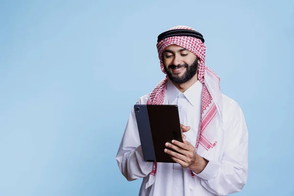 微笑的男人 头戴穆斯林头巾 手持数码平板电脑 在触摸屏上轻拍 阿拉伯人在带着愉悦表情的便携式小玩艺儿上滚动网页 — 图库照片