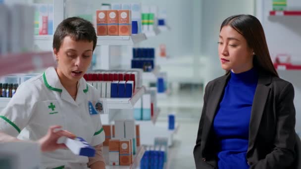 年次検査を終えた後 患者と薬局で薬剤師を経験し 病気の症状を治療する彼女の医療製品を示唆しています 医療従事者から治療を受けているアジア人女性 — ストック動画