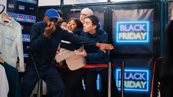 stock image Black friday shoppers argue at entrance to catch promotional prices on clearance items, angry people eager to start shopping. Mall customers pushing security man, asking him to open store.