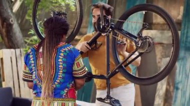 Spor düşkünü, ırklar arası bir çift, her yıl evlerinin bahçesinde bisiklet bakımı yapıyor. Afrika kökenli Amerikalı kadın, tamir standında özel ekipman ayarlarken, elinde bisiklet tutan aktif beyaz bir adam..