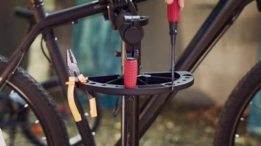 Bisiklet bakım faaliyetlerinin gerçekleşmesi için tamir standına dikkatlice yerleştirilmiş ince ayarlanmış aletlere yakından bir göz atın. Bisiklet servisi için ekipman düzenleyen adam.