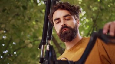 Atletik beyaz adam bisiklet pedalı ve krank kolunu doğru şekilde ayarlıyor. Uygun erkek bisikletçi, hasarlı bisikleti kontrol ediyor. Profesyonel tamir standında onarmaya hazır. Dolly zoom yap.