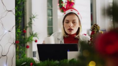 Noel süslü ofisinde bilgisayar ekranına bakıp kahve içen odaklanmış bir kadın. Çalışkan çalışanlar çeşitli xmas araştırmaları yapıyorlar. Bayram döneminde işyerlerini süslüyorlar.