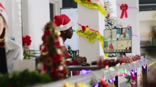 オンラインビデオコールのアフリカ系アメリカ人労働者は 同僚のクリスマス装飾オフィスに耳を傾ける お祝いの飾られた職場の管理幹部との遠隔電気会議のためのウェブカムを使用する従業員 — ストック動画