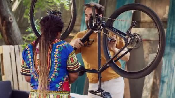 爱好运动的跨种族夫妇在自家院子里进行一年一度的自行车维修 活跃的高加索男子骑自行车 而非洲裔美国妇女则在维修站上安排专用设备 — 图库视频影像