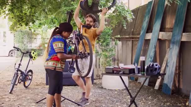 两名运动员与专业设备一起工作 修理和维护损坏的现代自行车 多族裔夫妇在自家院子里拆卸和修理自行车轮 — 图库视频影像