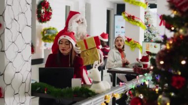 Noel Baba gibi giyinmiş bir meslektaşım, Noel neşesini Noel süsleme ofisine yayıyor ve personel üyelerine hediyeler sunuyor. Şenlikli çalışma alanında kostüm giyen, çok ırklı ve Noel hediyeli sürpriz bir takım.