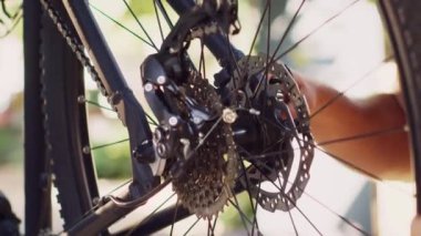 Bisikletinin kasetini bağlayan ve yıllık bakım için ayarlayan beyaz bir adamın açık havada yakın çekimi. Arka bahçesinde bisiklet tekerleğini inceleyen sportif erkek bisikletçinin detaylı görüntüsü..