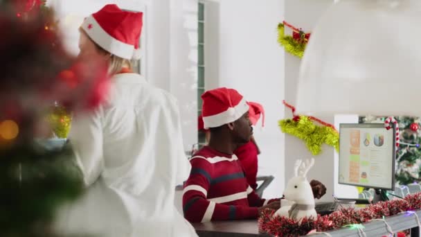 戴着圣诞老人帽的非裔美国人在圣诞华丽的办公室里工作 感到很疲倦 工作人员一边喝咖啡 一边查看圣诞节装饰工作场所的营业收入数字 — 图库视频影像